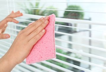 Person cleaning wooden blinds with a gentle cloth and mild soap